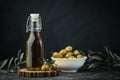 Green olives in a white bowl next to a bottle with olive oil and leaves on a black background. Bottle of cold pressed oil. Royalty Free Stock Photo