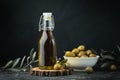 Green olives in a white bowl next to a bottle with olive oil and leaves on a black background. Bottle of cold pressed oil. Royalty Free Stock Photo