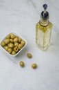 Green olives in a white ceramic bowl and glass bottle of olive oil on a light concrete background. Top view Royalty Free Stock Photo