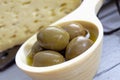 Green olives in wooden bowl cheese in background, close up