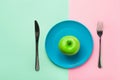 Green organic apple on blue plate with fork and knife on duotone chartreuse pink background. Healthy diet weight loss