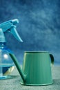 A green painted metal mini watering can with clear water spray on a green and blue background