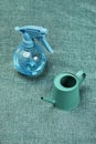 A green painted metal mini watering can with a spray of clear water on a green cloth background