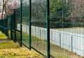 green painted metal wire fence between steel circular posts with sport field beyond.