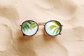 Green palm leaves reflecting in sunglasses on beach, top view