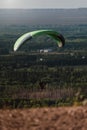 Green paraglider above tree fields