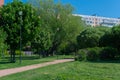 Green park with grass, trees, walking path, footpath, trail with lamps, street lanterns in front of a multi-storey buildings,