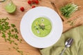 Green pea soup in a white plate. Cream soup on wooden table. Flat lay: soup, peas, tomatoes.