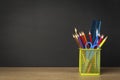 Green pencil holder with stationary supplies against blank black chalkboard, back to school concept Royalty Free Stock Photo