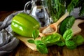 A green pepper, brans in a wooden spoon, basil, tarragon, a cucumber and water in a glass jug.