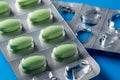Green pills in a blister pack on a blue background, close-up. Healthcare concept, drug addiction. Overuse of medication
