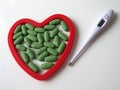 Green pills and an electric thermometer on white background