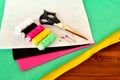 Green, pink, yellow, white and black felt sheets. Scissors, thread and pins on a wooden table