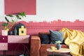 Green plant in white pot next to black and gold vases on pastel pink and burgundy shelf in living room with ombre wall and brown