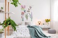 Green plants on shelves beside a bed dressed in white cotton bedding and teal blue blanket in a bright bedroom interior Royalty Free Stock Photo