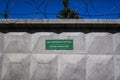 Green plaque with inscription CUSTOMS CONTROL ZONE in Russian and English on concrete wall with view of barbed wire and blue sky.