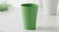 A green plastic cup stands upright on a white surface. To the right, a blurred white cup Royalty Free Stock Photo