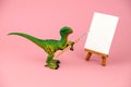 plastic dinosaur toy holding artistic brush and standing near mock up canvas, creative conceptual still life on a pink