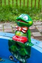 A green plastic frog with a tube in his mouth on the edge of a fountain on a clear sunny day. Playgrounds, sports, health Royalty Free Stock Photo