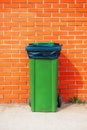 Green plastic garbage can against orange brick wall Royalty Free Stock Photo