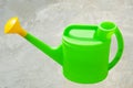 Green plastic watering can with yellow nozzle on gray concrete background. Watering pot is the simplest tool for drip Royalty Free Stock Photo