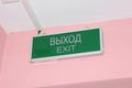 Green plate with the inscription exit in English and Russian on a pink wall