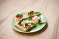 Green plate with salmon sandwiches with butter and parsley on wooden table. Buffet breakfast lunch meal. Healthy eating. Fish diet