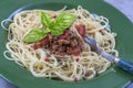 Green plate of Traditional Italian spahgetti Bolognaise or Bolognese with cooked pasta noodles topped with a tomato