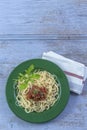 Green plate of Traditional Italian spahgetti Bolognaise or Bolognese with cooked pasta noodles topped with a tomato