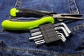 Green pliers and a metal multi-faceted wrench lies on a denim dark fabric close-up