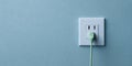 A green plug is plugged into a white electrical outlet on a blue wall Royalty Free Stock Photo