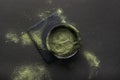 Super food or marijuana kief concept.Green powder in a small ceramic bowl, on a stone stand, on a black background.