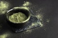 Green powder in a small ceramic bowl, on a stone stand, on a black background. Super food or marijuana kief concept