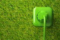 Green power cord in wall socket on grass background with copy space - eco or green power consumption concept Royalty Free Stock Photo