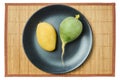 Green radish and yellow mango on a gray plate on a cane serving mat