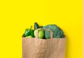 Green raw organic vegetables fruits broccoli cucumbers bell peppers apples in brown paper Kraft grocery bag on yellow background Royalty Free Stock Photo