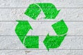 Green recycle symbol painted on a white natural textured wood.