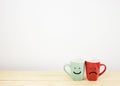 Green and red coffee mug with smile and sad face on wooden table Royalty Free Stock Photo