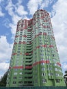 A green-red high-rise building stands against the background of a beautiful blue sky with clouds Royalty Free Stock Photo