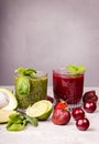 Green and red smoothie of strawberry, sweet cherry, avocado, spinach, basil, lime, green apple on gray background Royalty Free Stock Photo