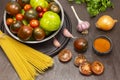 Green and red tomatoes in bowl. Pasta, chopped tomatoes, onion and garlic on table