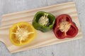 Green, red and yellow bell pepper halves over wooden board