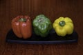 Green, red, yellow bell peppers on black platter. Dark background Royalty Free Stock Photo