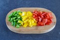 Green, red and yellow sweet paprika cut in cubes on a wooden cutting board on a dark abstract background. Step by step Royalty Free Stock Photo