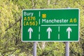 green and white street sign amongst a background of trees with directional guides on the A6 towards manchester or bury Royalty Free Stock Photo