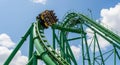 A roller coaster train with passengers crests a steep green track against a bright blue sky with white clouds Royalty Free Stock Photo