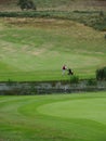 a green rolling golf course with a lake and a single golfer pushing his trolley