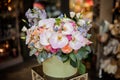 Green round box full of different tender color roses, orchids and bellflower decorated with green leaves