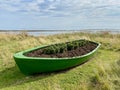 Green Rowing Boat Planter on grass with sea behind. Scottish Coast.