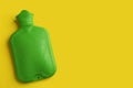 Green rubber hot water bottle on yellow background, top view. Space for text Royalty Free Stock Photo